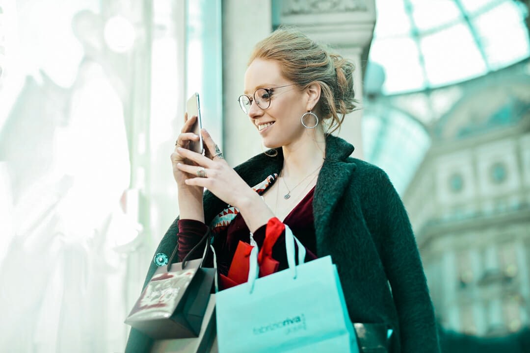 woman with shopping bags taking photos with her phone outdoors