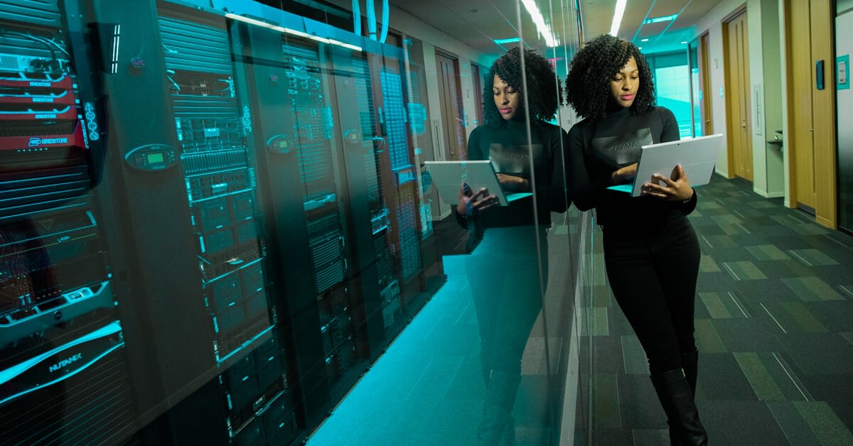 female employee of a software development company posing with her laptop while leaning on the glass wall of a data storage room