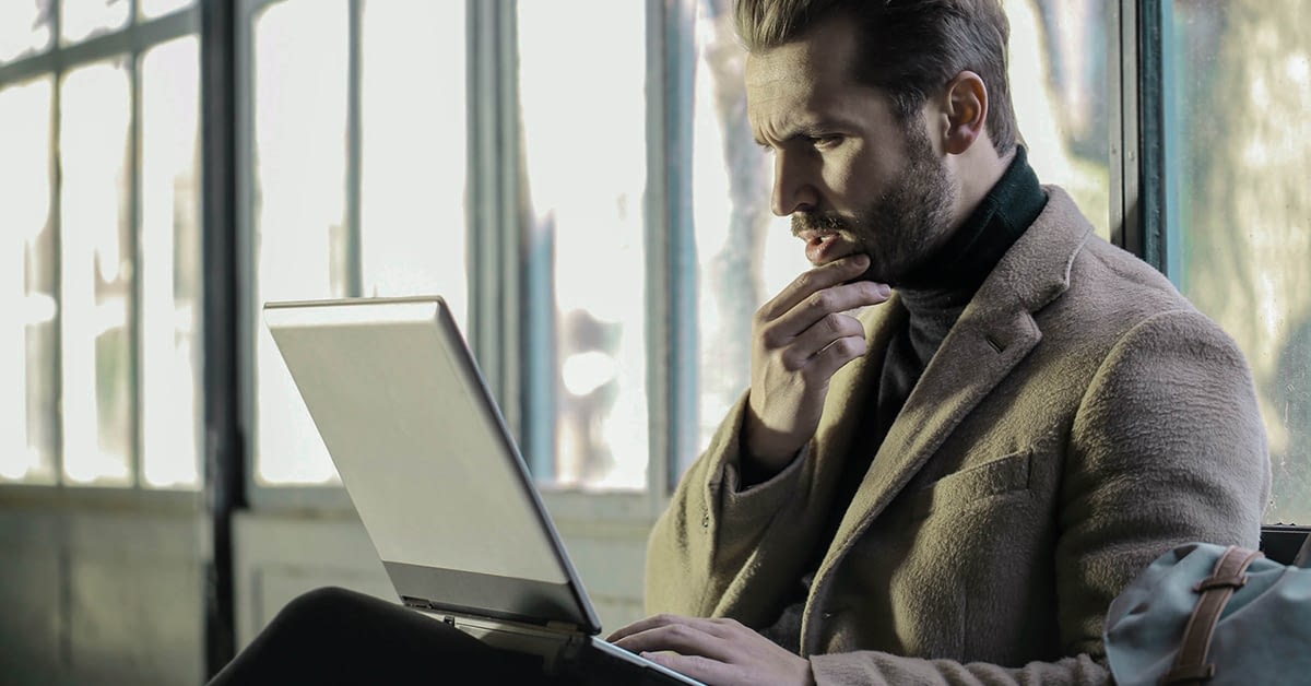 perplexed businessman holding his chin while looking into his laptop about business process outsourcing
