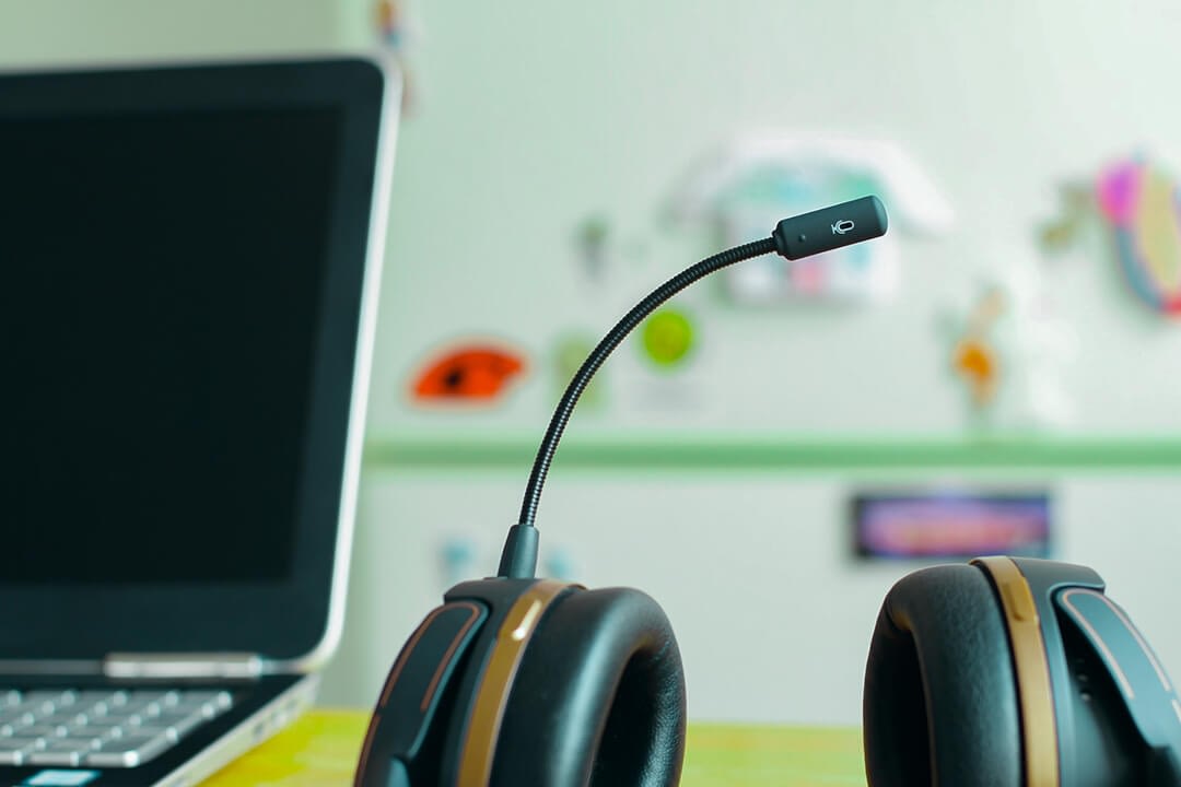close up photo of a headset beside a laptop on a desk