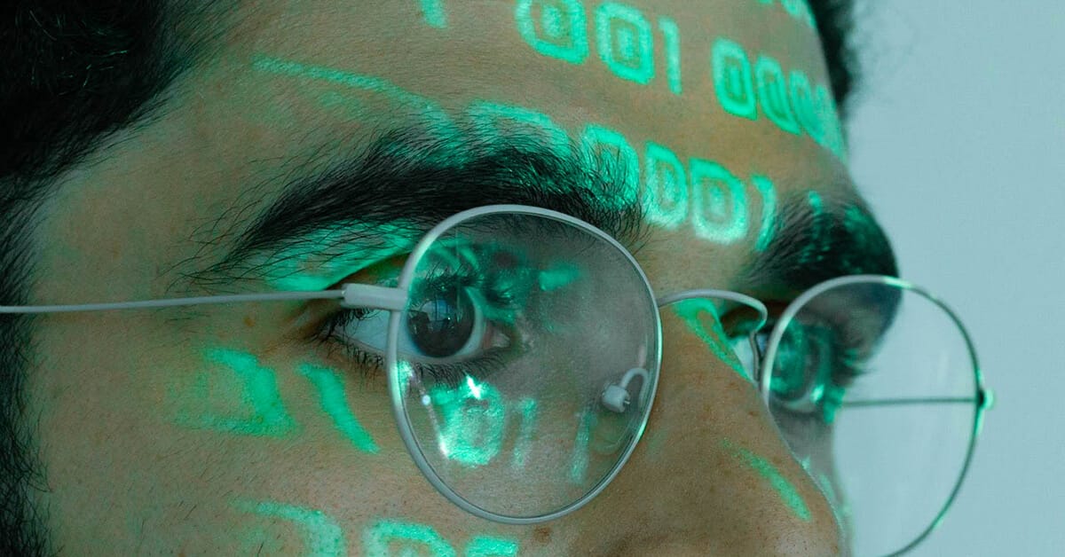software development image, close up view of a man's face with streaks of green reflections of computer codes